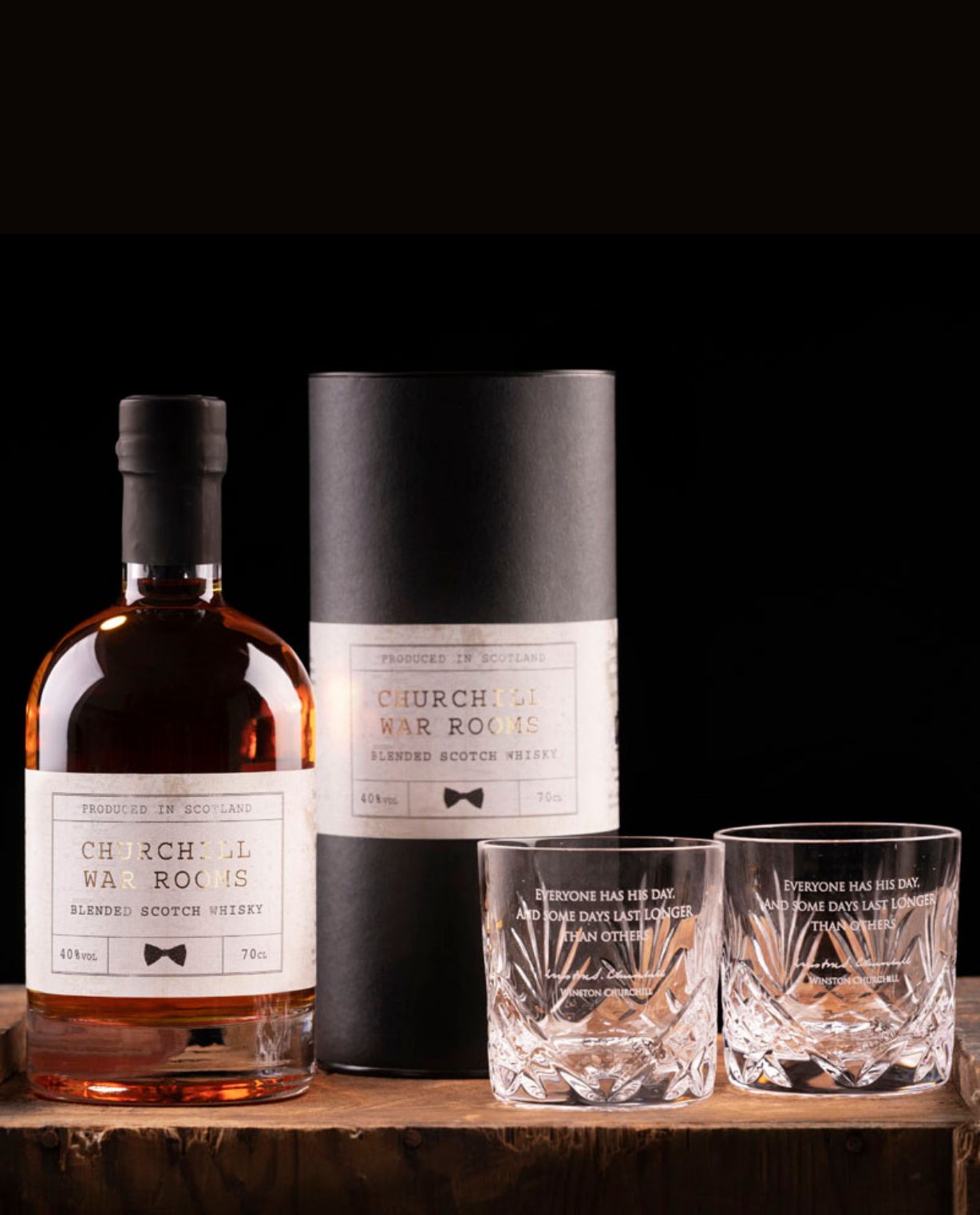 Bottle and packaging of Churchills War Room whisky with two glasses on a wooden surface.