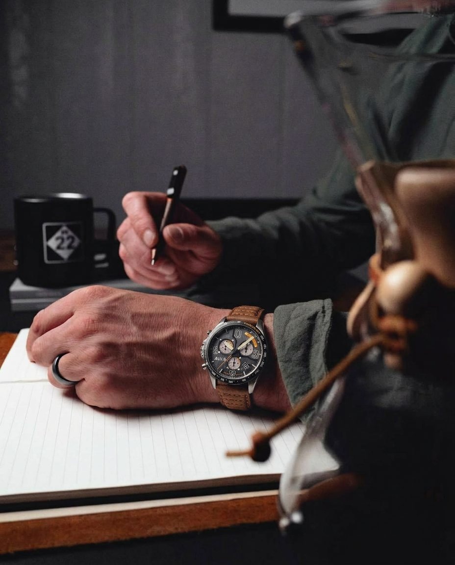 Person writing in a notebook with a watch on their wrist, wearing a green jacket.
