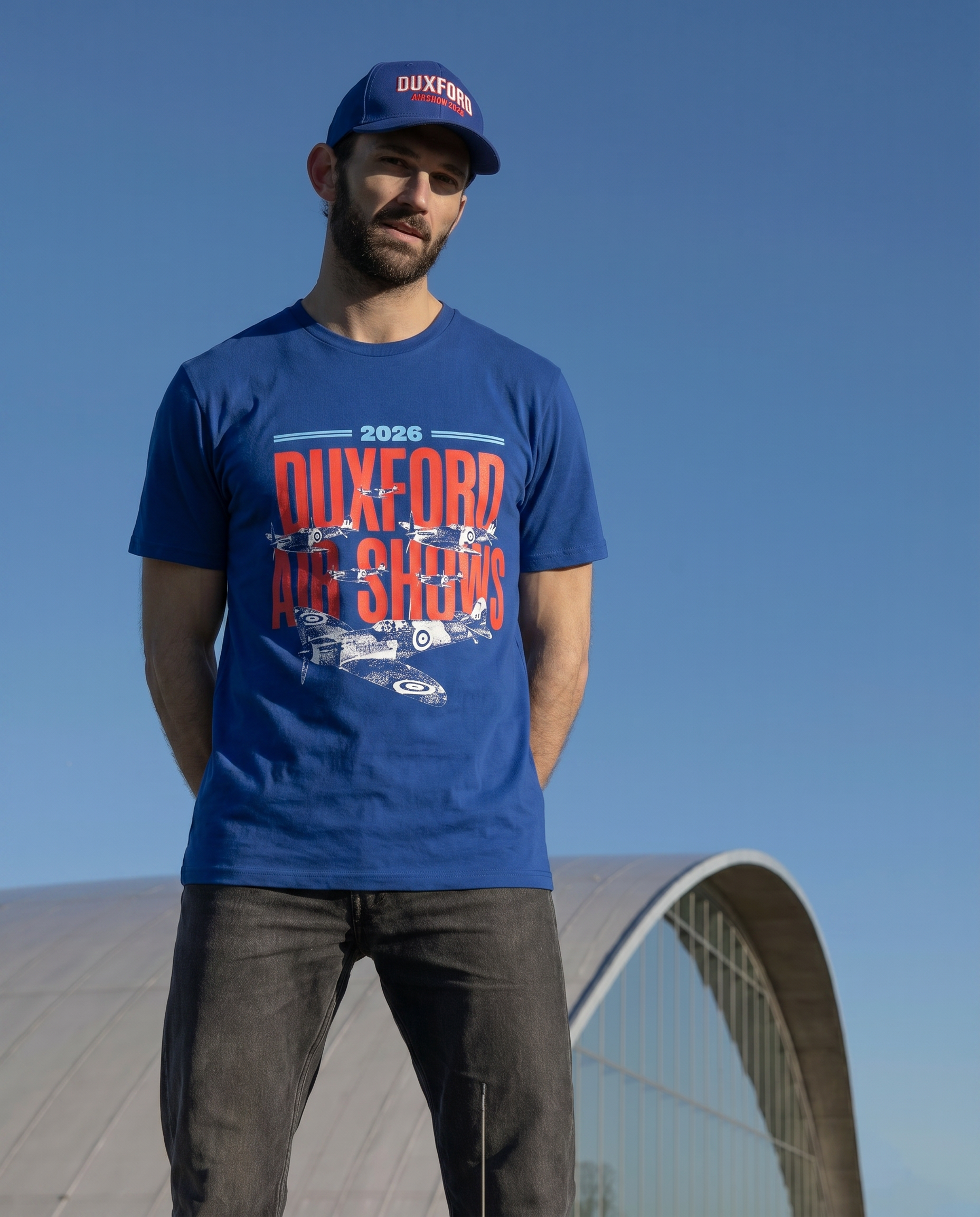 Man wearing a blue t-shirt with 'Duxford Air Shows' text and a cap, standing against a clear blue sky.