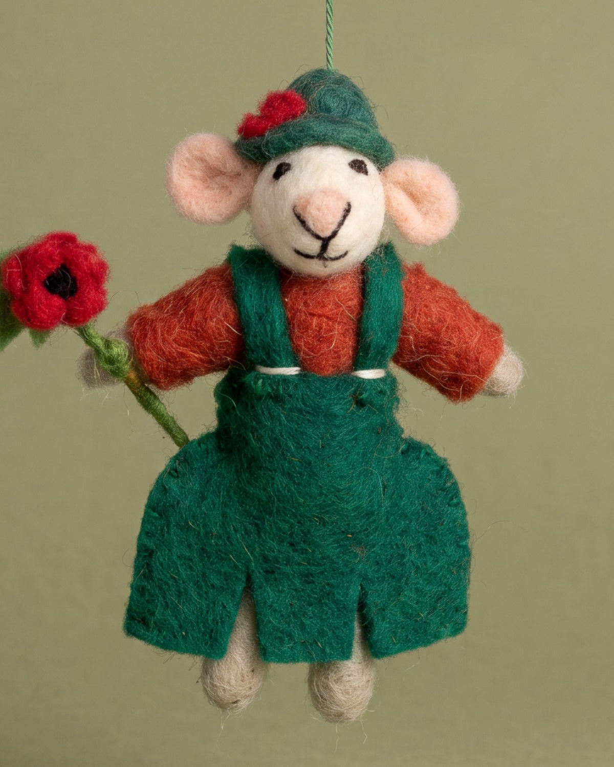 A handcrafted felted wool mouse ornament wearing a green hat and overalls with an orange-brown shirt, holding a red poppy flower, set against a solid olive green background.