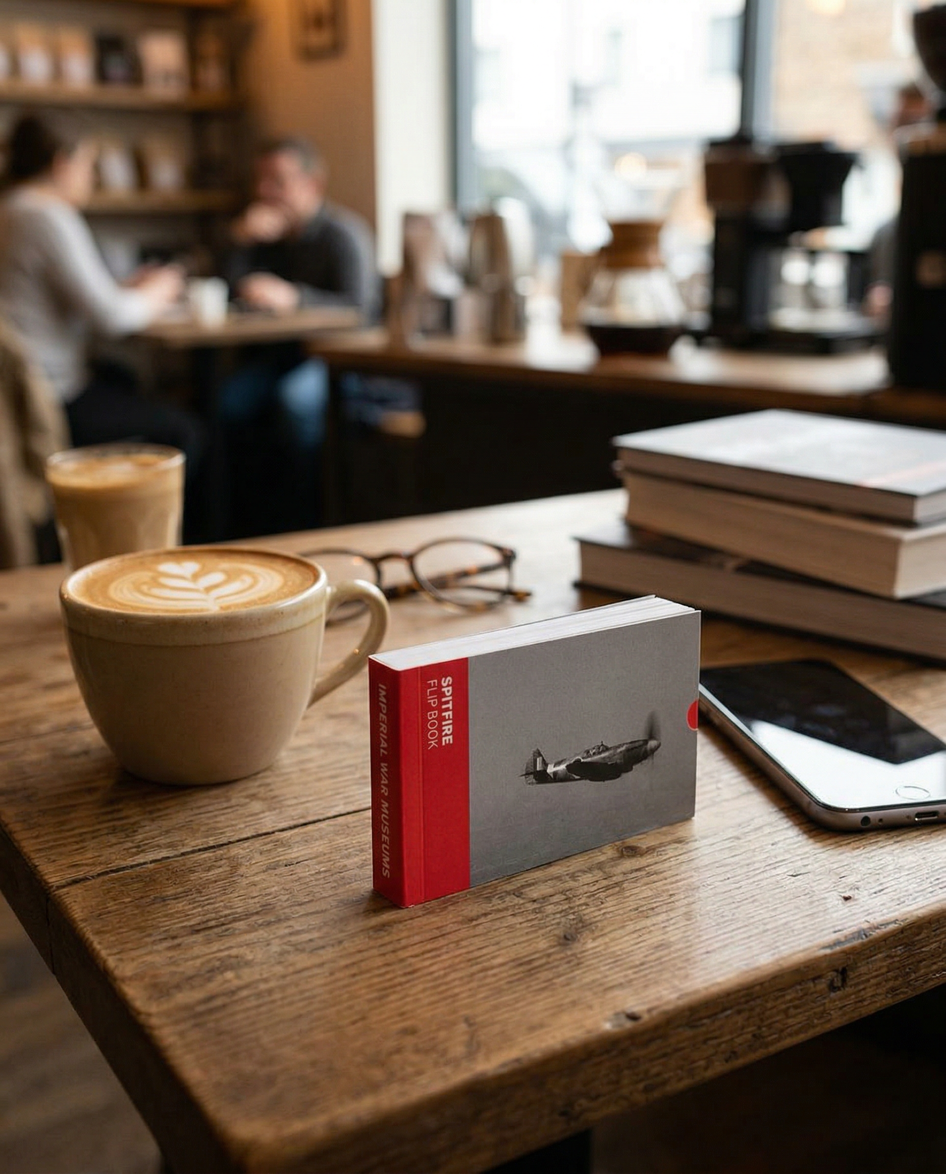 Cappuccino in a mug, book, and smartphone on a wooden table in a coffee shop.