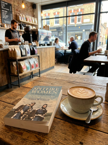 Book titled 'Spitfire Women' on a table with a coffee cup in a cafe setting