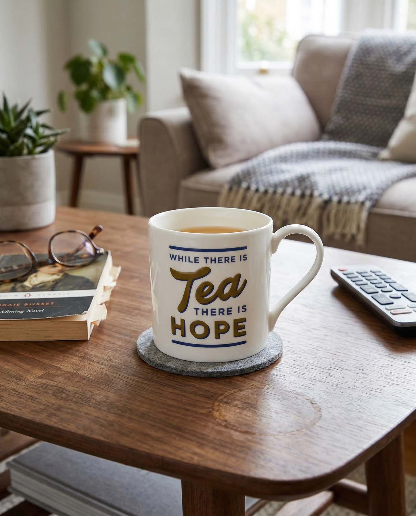 Mug with 'While there is tea, there is hope' text on a wooden table in a cozy living room.